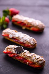 individual eclair pastry filled with strawberries on a black marble backdrop 