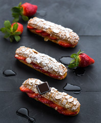 individual eclair pastry filled with strawberries on a black marble backdrop 