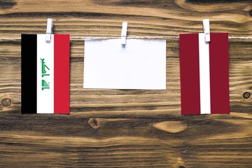 Hanging flags of Iraq and Latvia attached to rope with clothes pins with copy space on white note...
