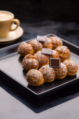 individual eclair pastry dusted with powder sugar on a black plate with a mug of coffee
