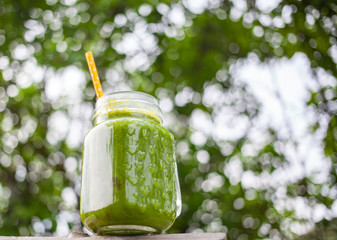  jar with green cold-pressed juice, vegetable garden background. Healthy eating, detoxing, juicing,...