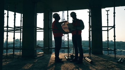 Constructions planning held by two construction engineers at the building lot - Powered by Adobe