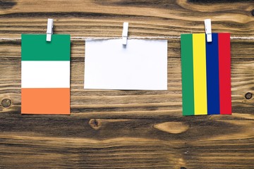 Hanging flags of Ireland and Mauritius attached to rope with clothes pins with copy space on white note paper on wooden background.Diplomatic relations between countries.