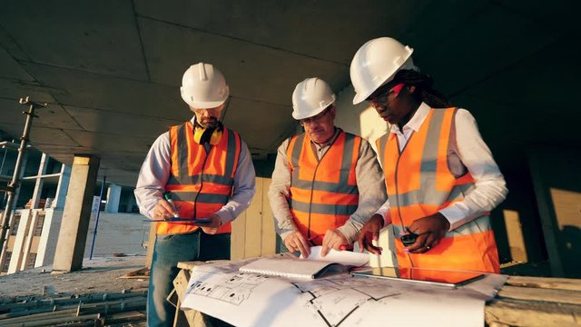 Group of engineers in safety wear are discussing layouts on a construction site.