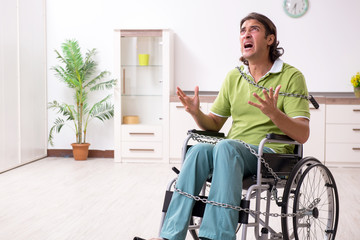 Young male invalid in wheel-chair suffering at home