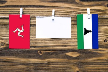 Hanging flags of Isle Of Man and Lesotho attached to rope with clothes pins with copy space on...