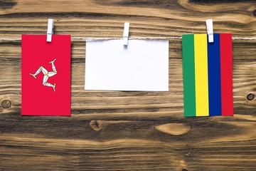 Hanging flags of Isle Of Man and Mauritius attached to rope with clothes pins with copy space on white note paper on wooden background.Diplomatic relations between countries.