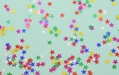 Festive background. Colorful glitter stars on mint color background.