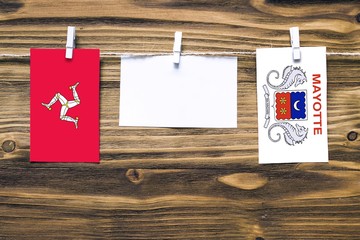 Hanging flags of Isle Of Man and Mayotte attached to rope with clothes pins with copy space on white note paper on wooden background.Diplomatic relations between countries.