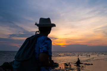 tourist with backpack of freedom on sand beach in silhouette of asian young woman relaxing, standing looking sunset scene in summer sky outdoor. journey trip outdoors in summer concept
