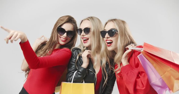 Happy smiling girlfriends in red fashionable clothing and sunglasses pointing fingers on new outfit, black friday sale