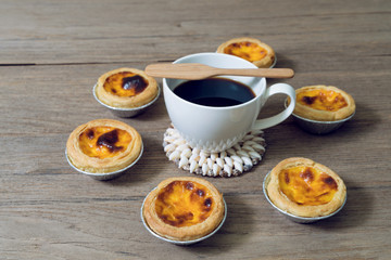 coffee with egg tart in aluminum foil cup on wood table