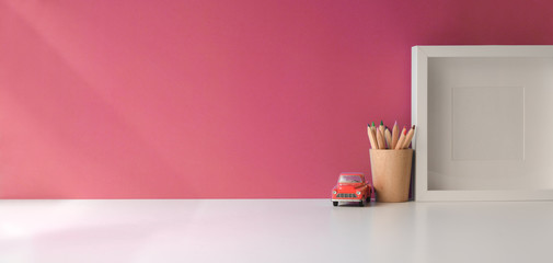 Modern workspace with mock up frame and copy space on white wooden table and pink wall