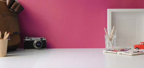 Stylish workspace with copy space, camera and office supplies on white table and pink wall