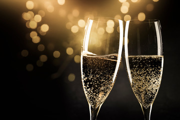 two champagne glasses ready to bring in the New Year - holiday lights and fireworks in the background