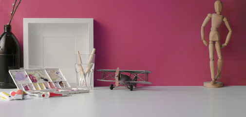 Professional artist workspace with painting tools and mock up frame with copy space on white table and pink wall