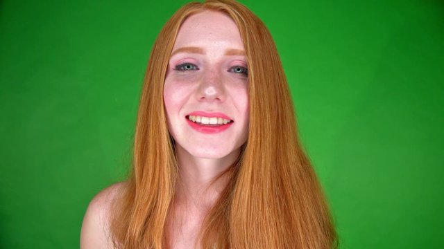 Against a green backdrop, a young women blows a kiss towards the camera