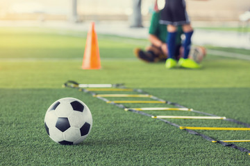 Soccer ball and ladder drills on green artificial turf with blurry kid football player and coach are training. Soccer training or football training equipment in academy.