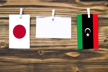Hanging flags of Japan and Libya attached to rope with clothes pins with copy space on white note...