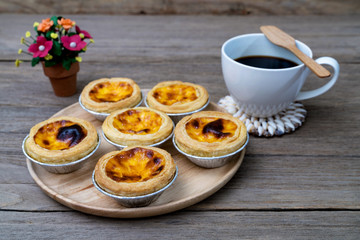 coffee with egg tart in aluminum foil cup on wood table
