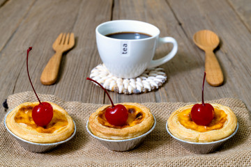 egg tart in aluminum foil cup with red cherry and coffee on wood table