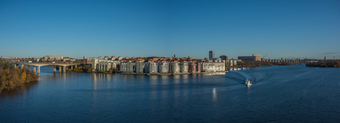 Naklejka premium Commuting boat and a sunny autumn view over Stockholm districts at the lake Mälaren Essinge, Kungsholmen and Långholmen island