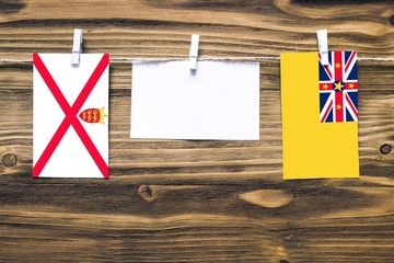 Hanging flags of Jersey and Niue attached to rope with clothes pins with copy space on white note paper on wooden background.Diplomatic relations between countries.