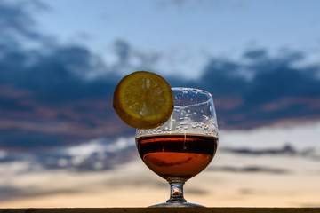 A glass of cognac with lemon on the background of the twilight	