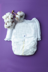 Stack of diapers Nappy and white cotton flowers on violet background.