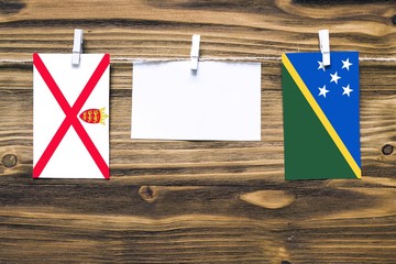Hanging flags of Jersey and Solomon Islands attached to rope with clothes pins with copy space on...