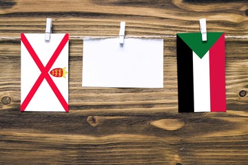 Hanging flags of Jersey and Sudan attached to rope with clothes pins with copy space on white note...