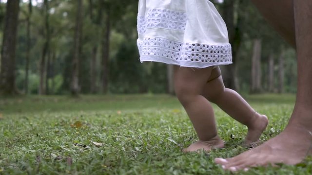 father support his daughter to walk her first step on grass
