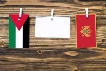 Hanging flags of Jordan and Montenegro attached to rope with clothes pins with copy space on white note paper on wooden background.Diplomatic relations between countries.