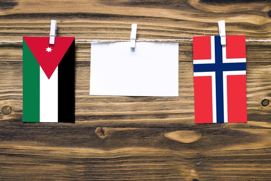 Hanging flags of Jordan and Norway attached to rope with clothes pins with copy space on white note paper on wooden background.Diplomatic relations between countries.