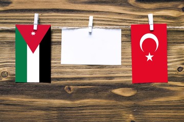 Hanging flags of Jordan and Turkey attached to rope with clothes pins with copy space on white note paper on wooden background.Diplomatic relations between countries.