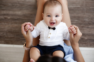 Mother and child on a white bed.Mom and baby boy in shorts playing in sunny bedroom. Parent and...