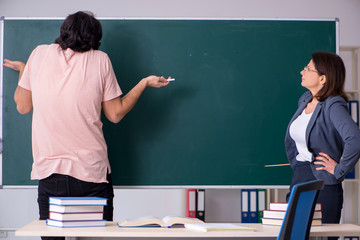 Old female teacher and male student in the classroom