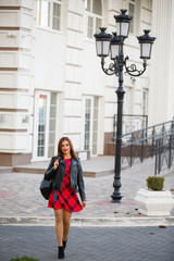 Young brunette girl weared in red dress and leather jacket on background of the City near old...
