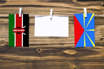 Hanging flags of Kenya and Reunion attached to rope with clothes pins with copy space on white note paper on wooden background.Diplomatic relations between countries.