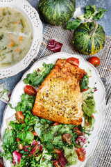 Salmon spiced with herbs, a plate of vegetable soup and a fresh salad.