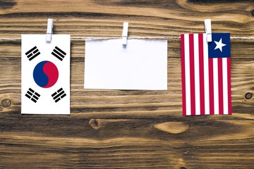 Hanging flags of South Korea and Liberia attached to rope with clothes pins with copy space on white note paper on wooden background.Diplomatic relations between countries.
