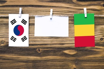 Hanging flags of South Korea and Mali attached to rope with clothes pins with copy space on white note paper on wooden background.Diplomatic relations between countries.