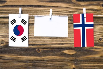 Hanging flags of South Korea and Norway attached to rope with clothes pins with copy space on white note paper on wooden background.Diplomatic relations between countries.