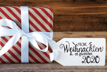 Fototapeta na wymiar One Christmas Gift With Label With German Calligraphy Frohe Weihnachten Und Ein Glueckliches 2020 Means Merry Christmas And A Happy 2020. Wrapping Paper With A Bow
