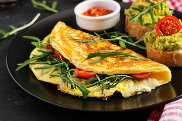 Breakfast. Omelette with tomatoes, cheese, green arugula and toasts with avocado cream on black plate. Frittata - italian omelet.