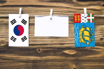 Hanging flags of South Korea and Saint Pierre And Miquelon attached to rope with clothes pins with copy space on white note paper on wooden background.Diplomatic relations between countries.