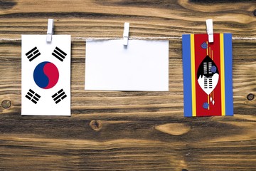Hanging flags of South Korea and Swaziland attached to rope with clothes pins with copy space on white note paper on wooden background.Diplomatic relations between countries.