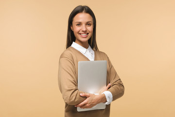 Fototapeta premium Female college student smiling at camera, holding laptop ready to go to studies, isolated on brown background