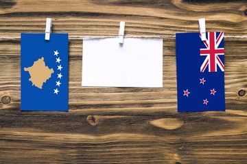 Hanging flags of Kosovo and New Zealand attached to rope with clothes pins with copy space on white note paper on wooden background.Diplomatic relations between countries.