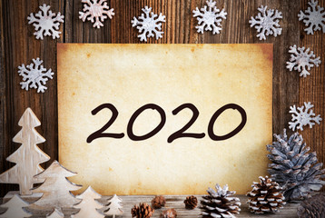 Fototapeta na wymiar Old Paper With Text 2020. Christmas Decoration Like Tree, Fir Cone And Snowflakes. Brown Wooden Background